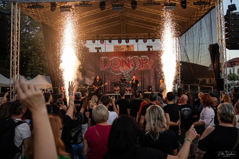Ohňová show na festivalovém pódiu, diváci s rukama nad hlavou